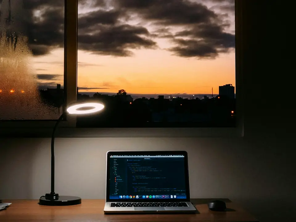 Laptop with code on a desk by a window at sunset